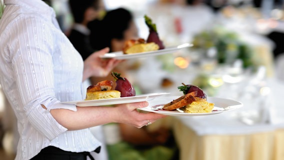Eine Kellnerin mit drei Tellern geht durch ein Lokal. © fotolia.com Foto: MNStudio